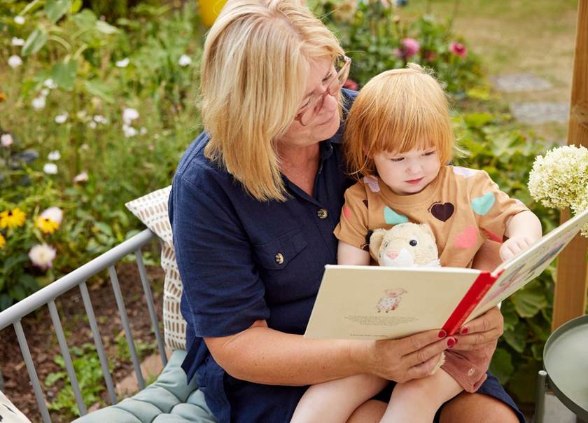 Grandmother sat reading to grandchild outside