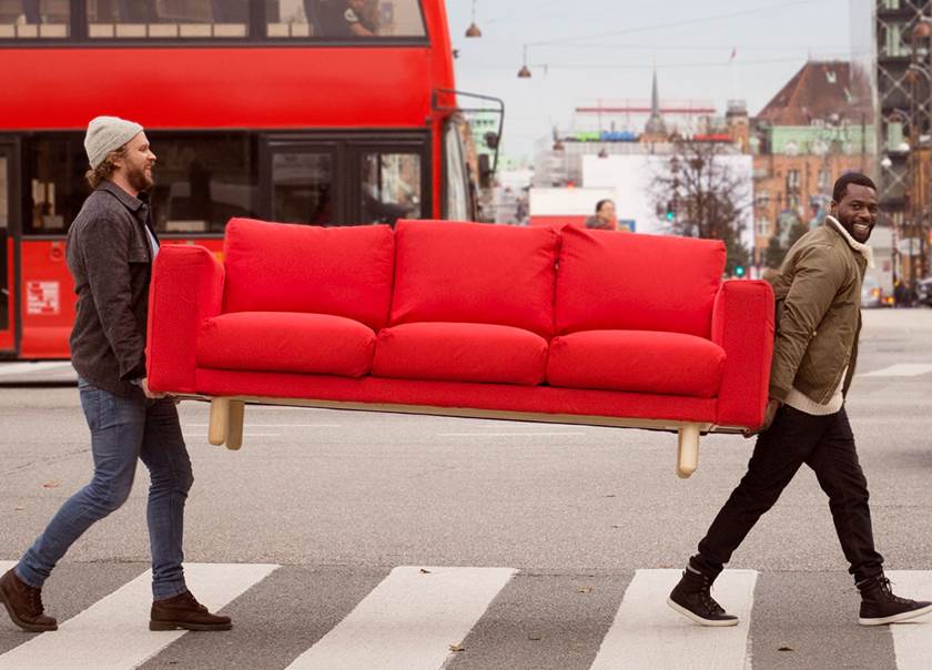Two men carrying a red sofa across a road