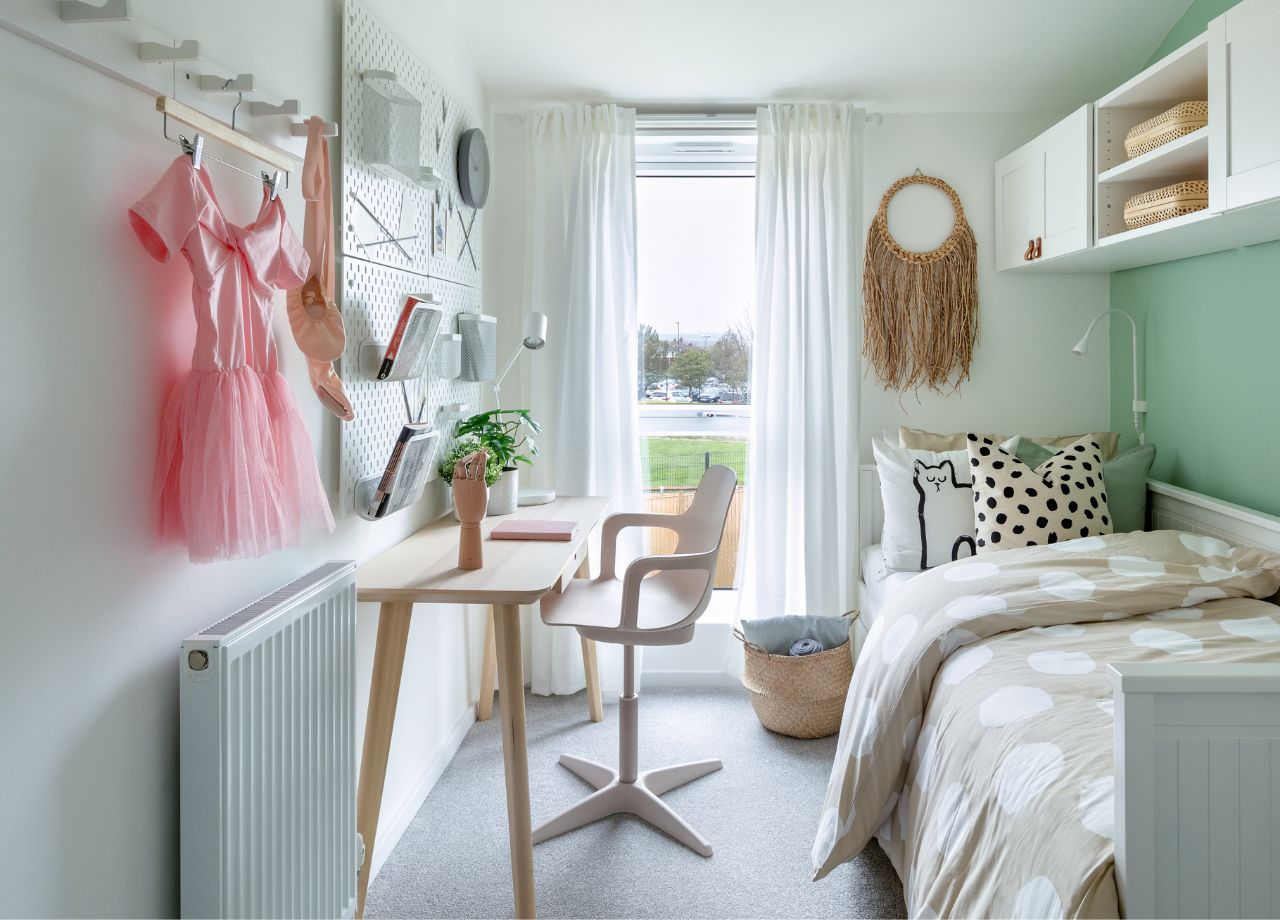 Shelves on a green coloured wall and a single bed with beige bed linen.