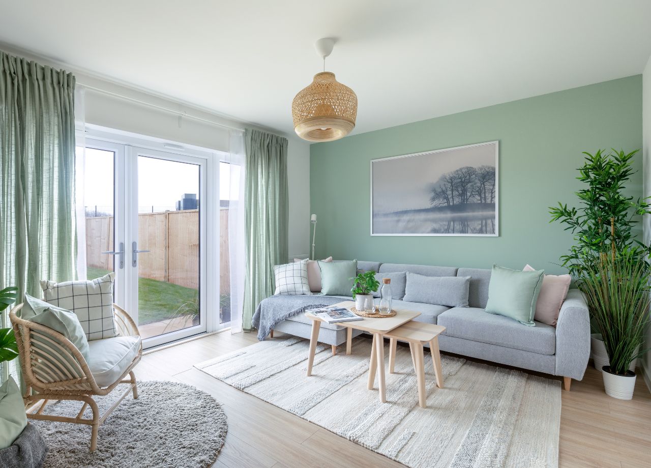 Internal lounge shot of a BoKlok home with green sofa filled with comfy pillows. In fornt of it stands two coffee tables in wood on a beige rug.